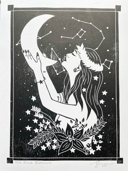 An A4 lino print of a women holding the moon up to her face with her hands, she's surrounded by stars and flowers