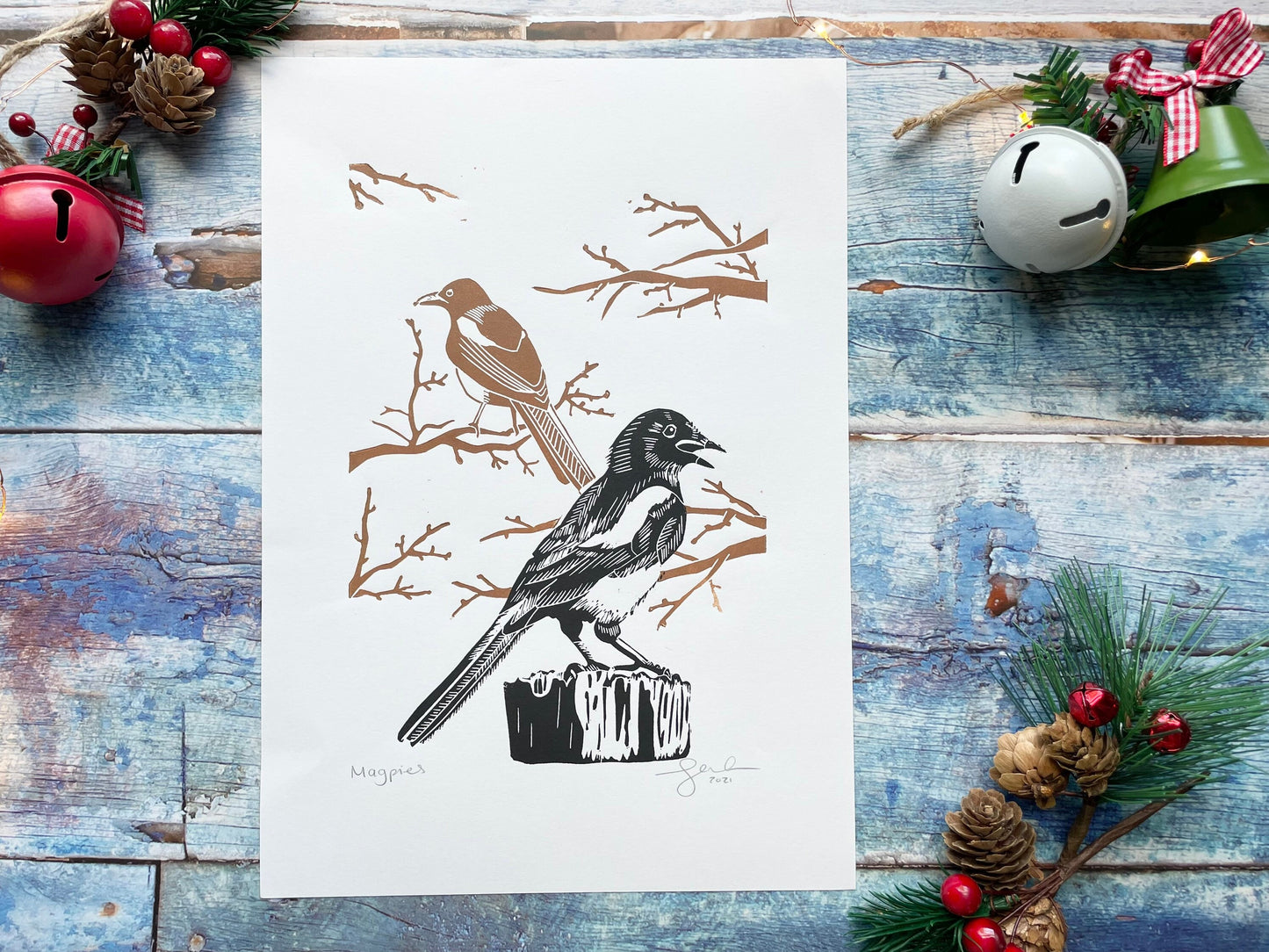 A mounted lino print of two magpies, the one in the foreground is black and the one in the background is brown