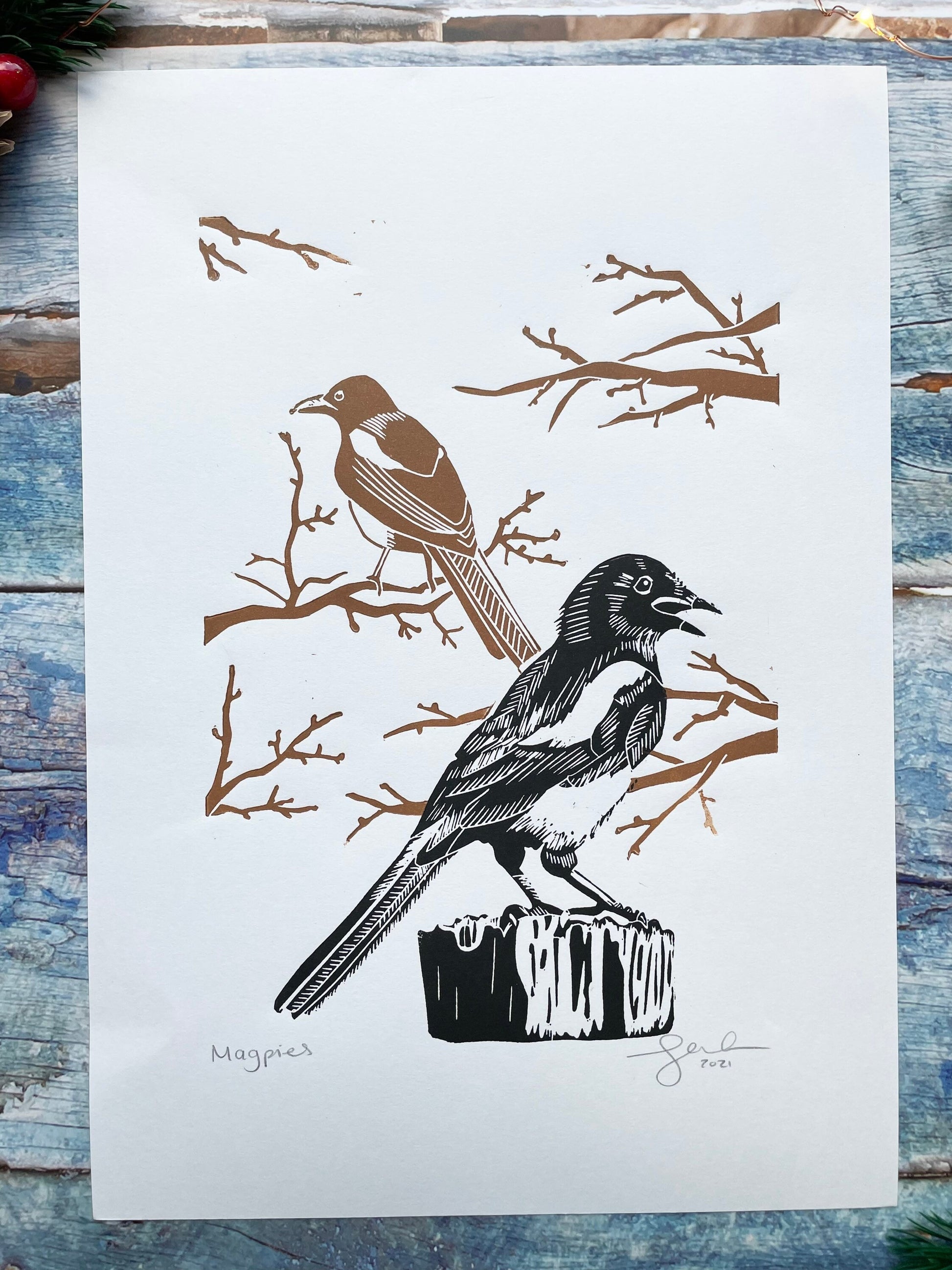 A mounted lino print of two magpies, the one in the foreground is black and the one in the background is brown