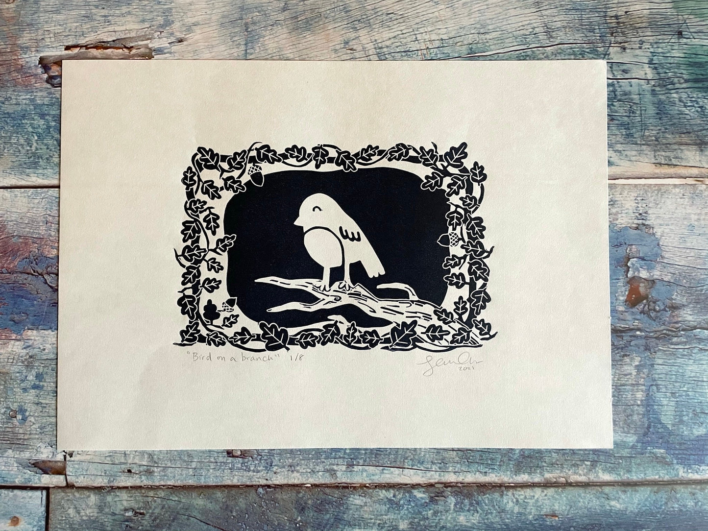 A small lino print of a robin on a tree surrounded by oak leaves and stars