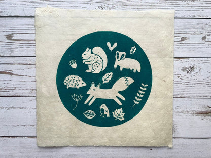 A circular lino print in green on gorgeous handmade mulberry paper. The print has woodland animals on it and fauna.