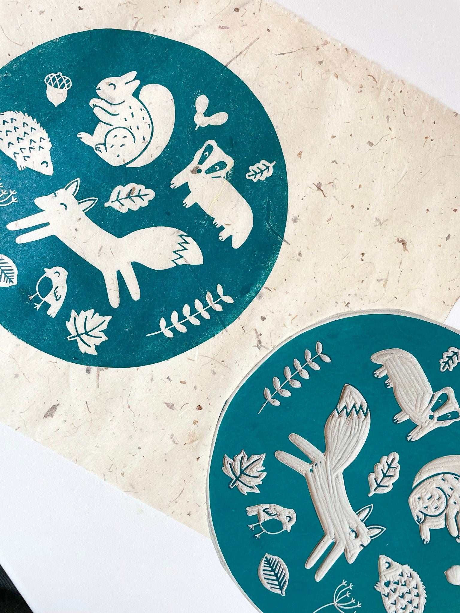 A circular lino print in green on gorgeous handmade mulberry paper. The print has woodland animals on it and fauna.