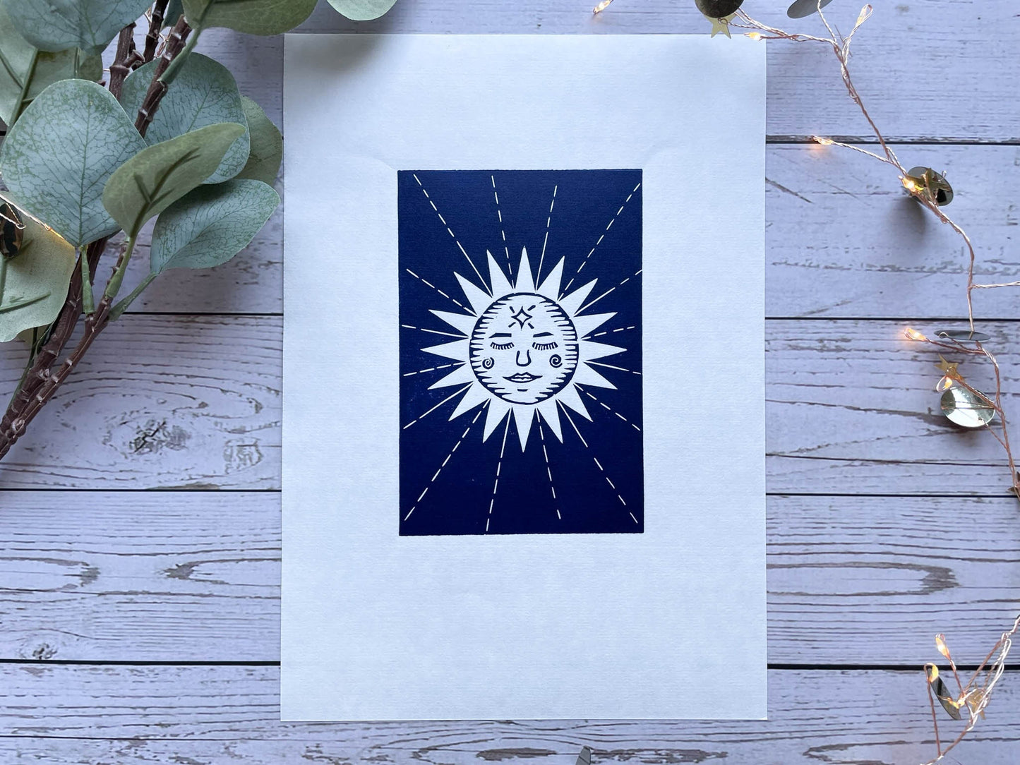 A lino print of a sun with a face and rays coming away from her.