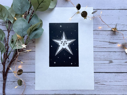 A lino print of a star with a face and surrounded by stars on A4 paper