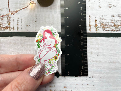 A 5cm sticker next to a ruler of a breastfeeding mother laying on a bed of flowers and leaves