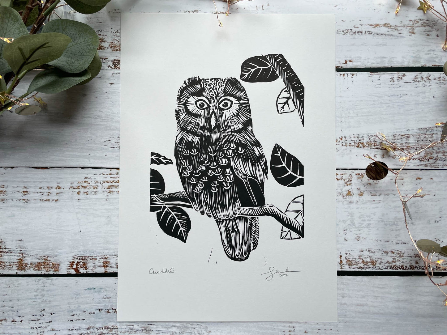A lino print of an owl sitting in a tree in black