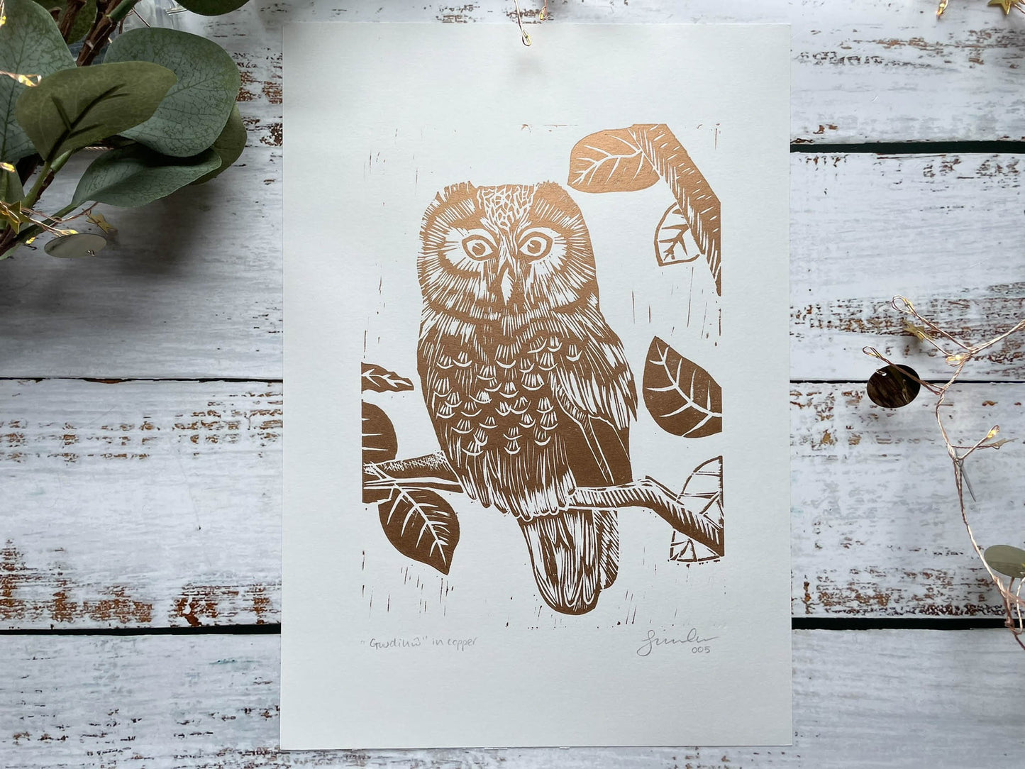 A lino print of an owl sitting in a tree in black in copper