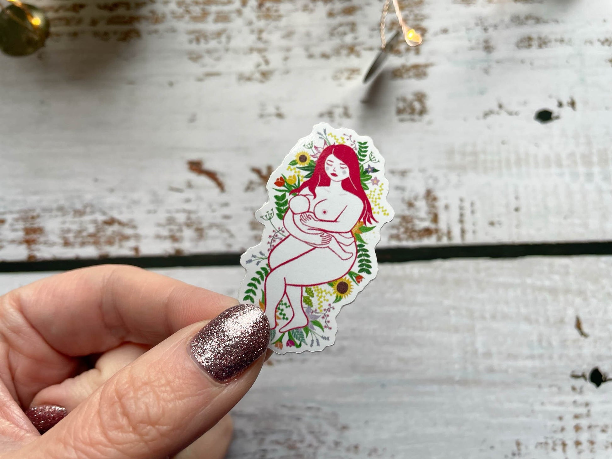 A 5cm sticker of a breastfeeding mother laying on a bed of flowers and leaves