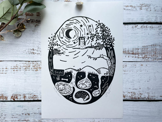 An oval lino print of an owl in a tree watching over the woodland animals while they sleep in black