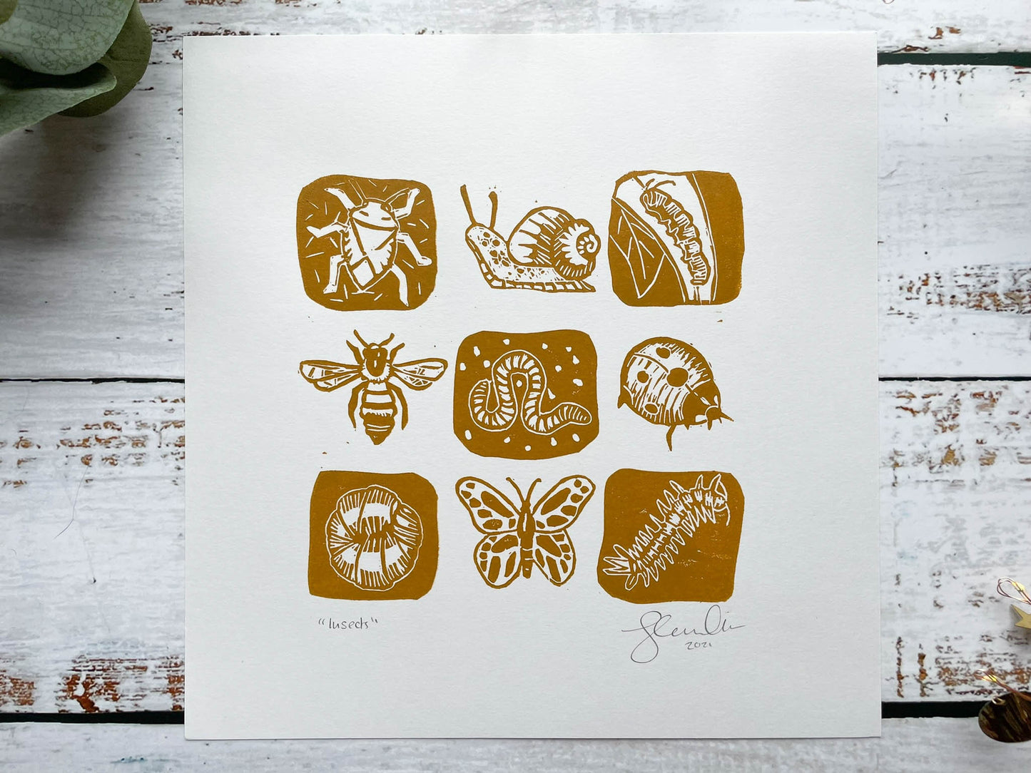 A lino print of a 3 x 3 grid of mini-beasts in yellow ochre