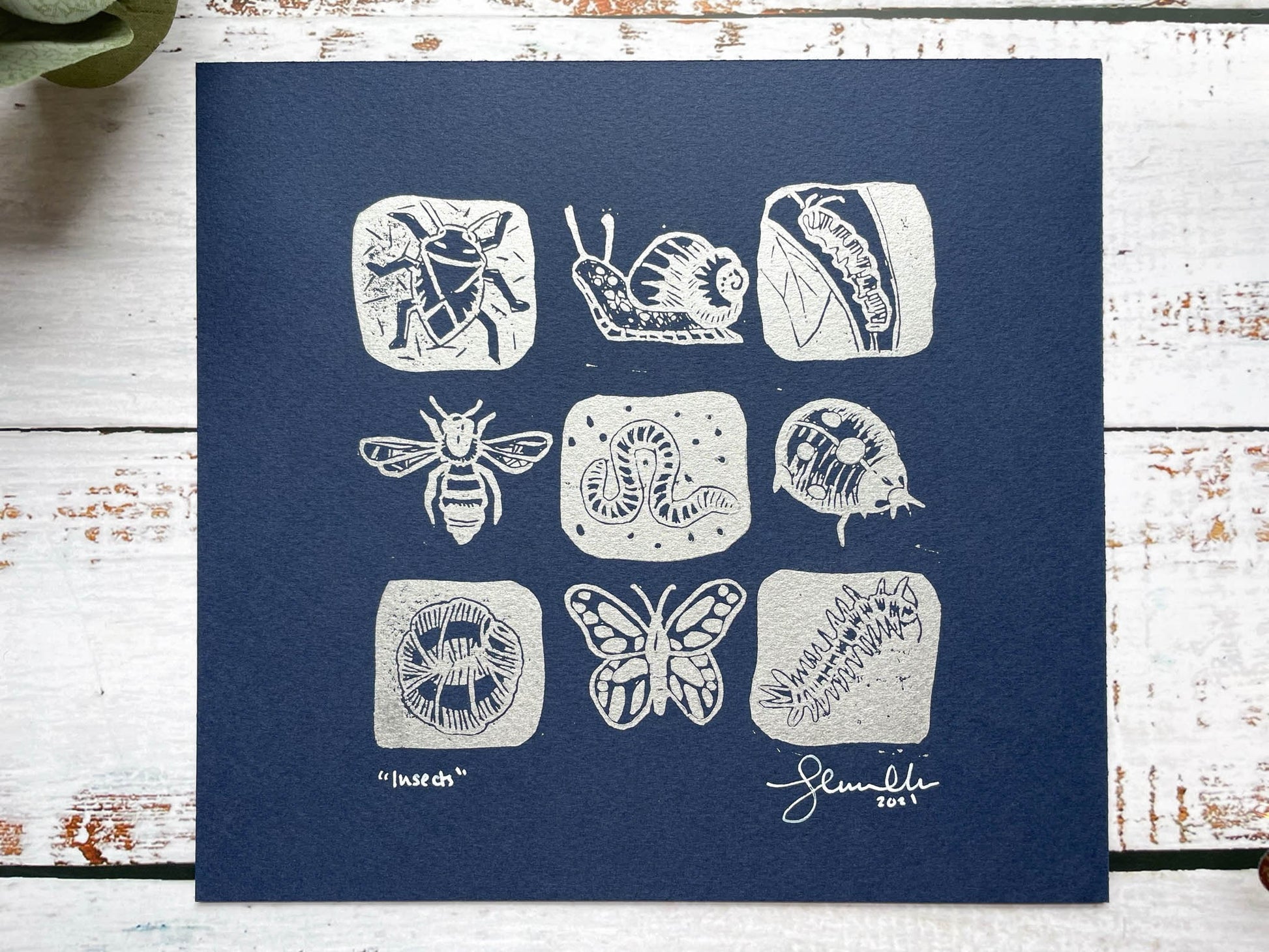 A lino print of a 3 x 3 grid of mini-beasts in silver on blue