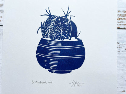 A small blue lino print of a little potted succulent