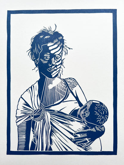 A blue lino print of a mother breastfeeding her baby in a ring sling with sunlight across her face through the blinds.