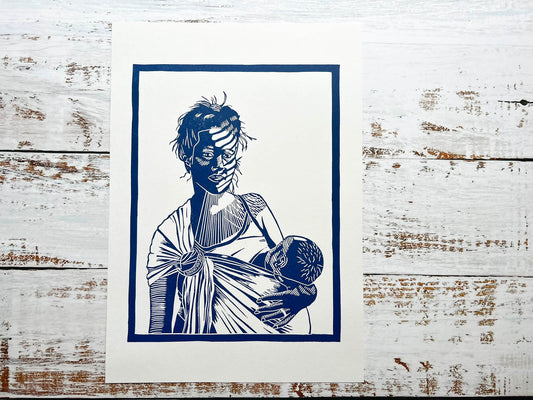 A blue lino print of a mother breastfeeding her baby in a ring sling with sunlight across her face through the blinds.