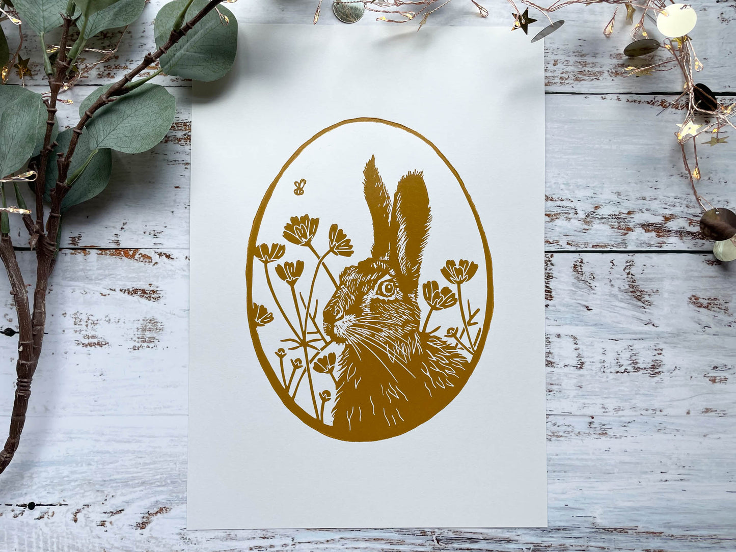 An oval lino print using yellow ochre of a hare surrounded by flowers on A4 paper